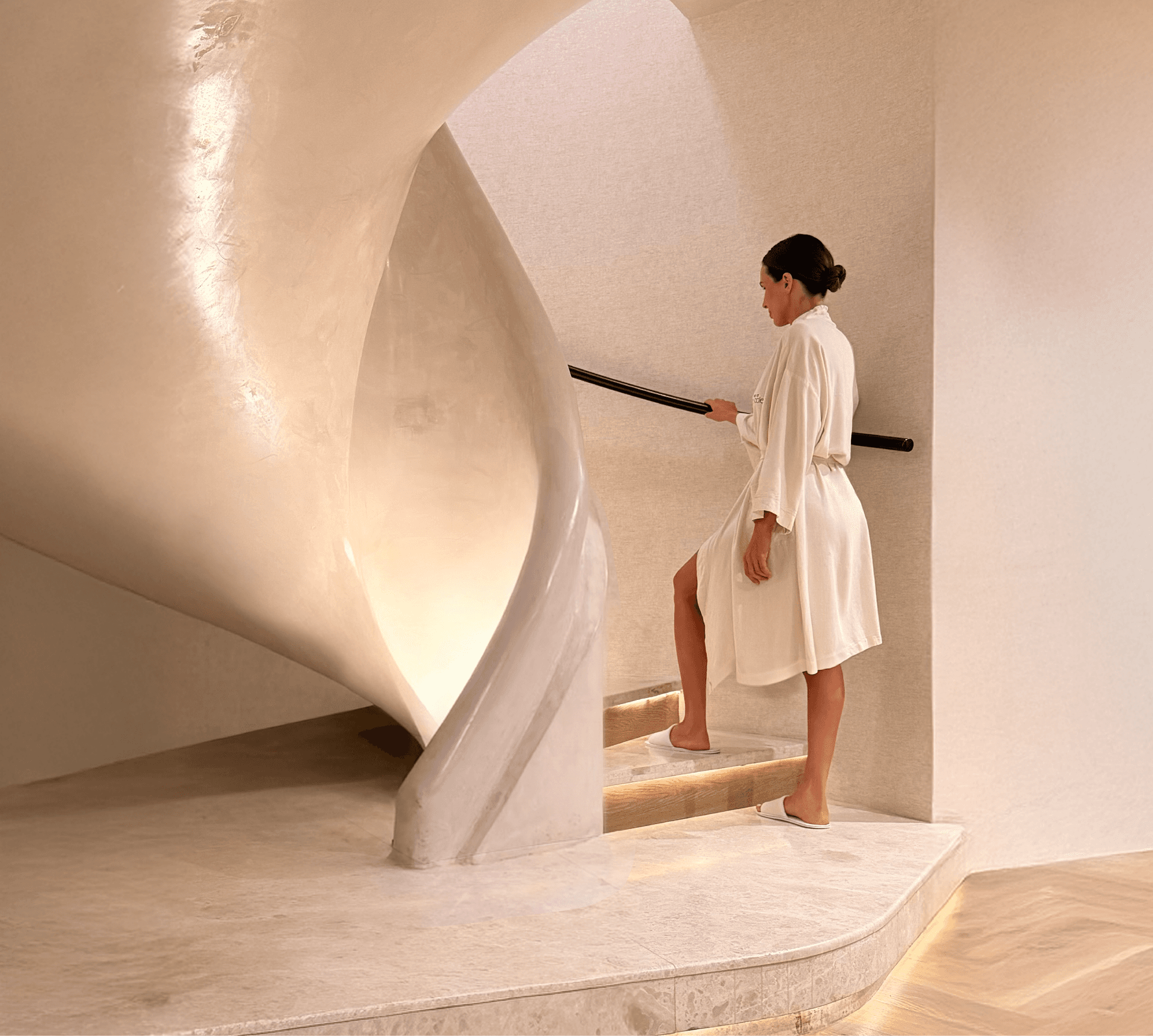 Guest in a robe descending the sculptural spiral staircase at Spa at The Cole, promoting the spring spa offer