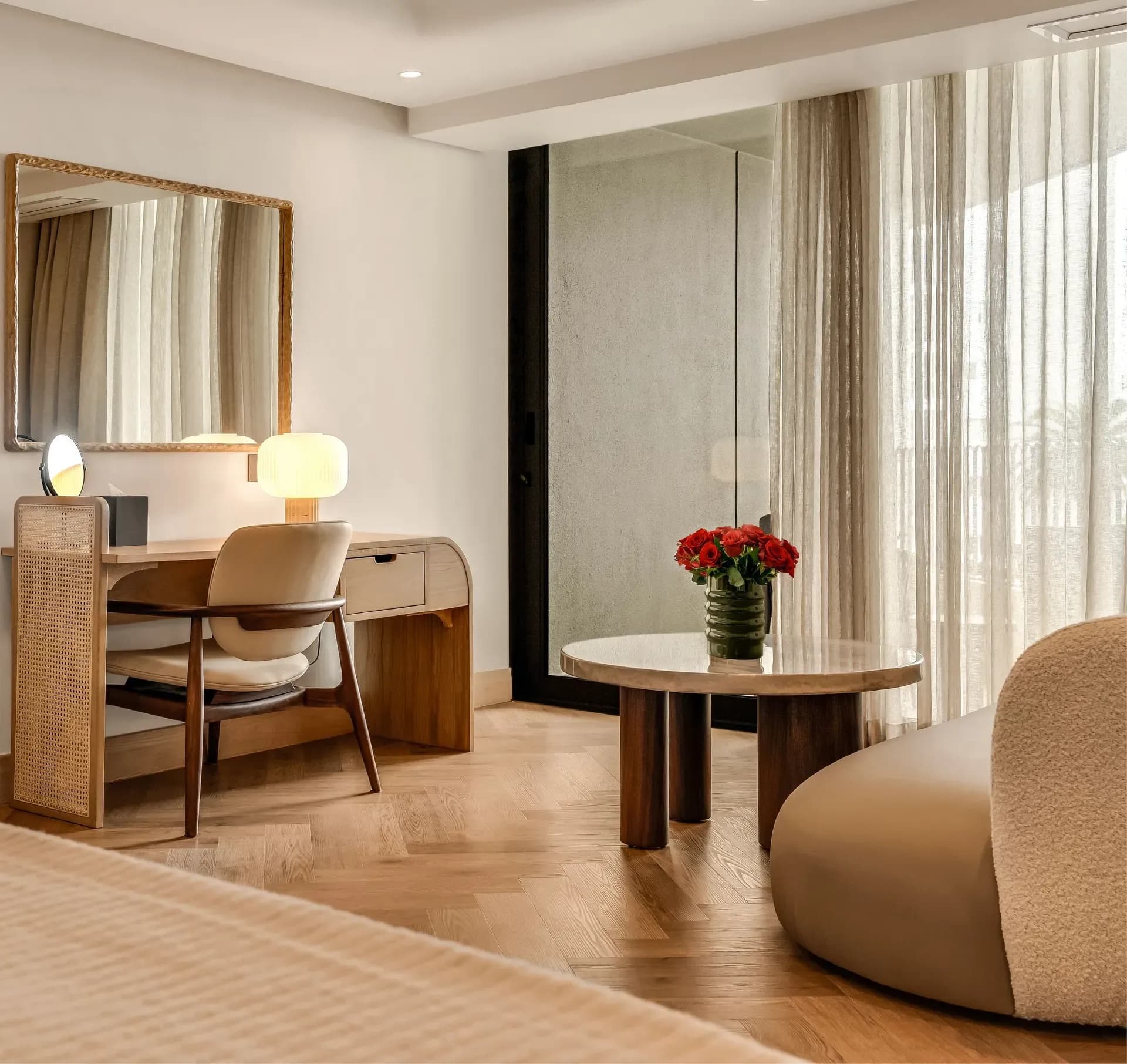 Classic Sea-Facing Room at The Cole featuring a cane-panelled wardrobe, wooden writing desk with table lamp, bouclé armchair, and sheer curtained balcony doors with natural light