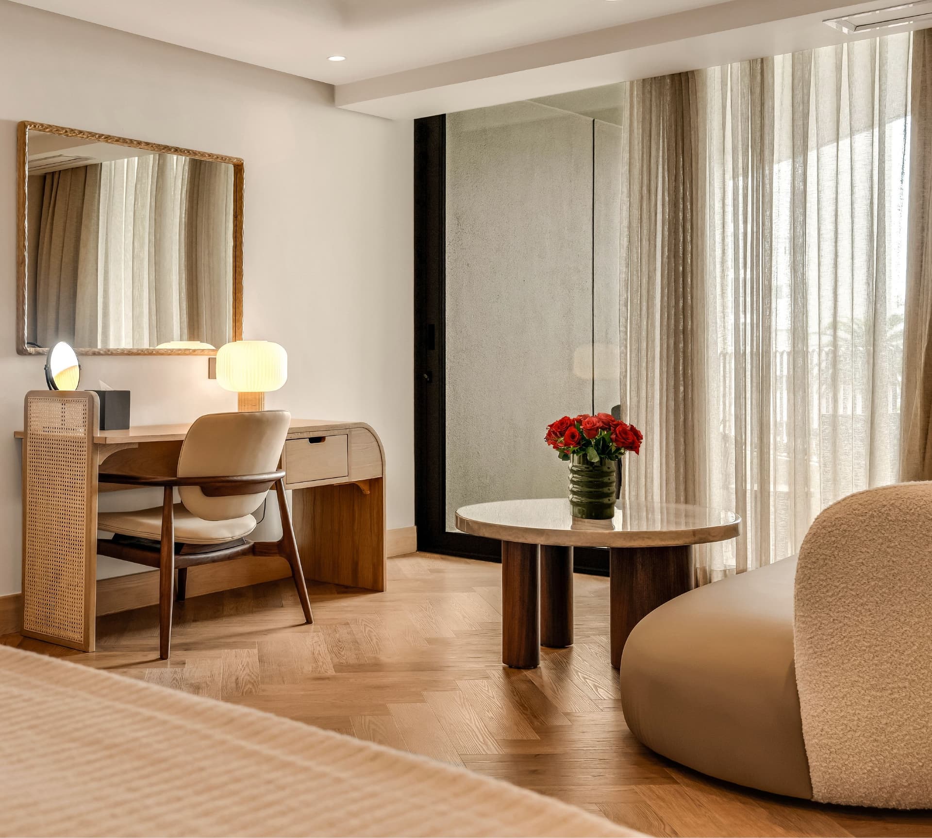 Classic Sea-Facing Room at The Cole featuring a cane-panelled wardrobe, wooden writing desk with table lamp, bouclé armchair, and sheer curtained balcony doors with natural light