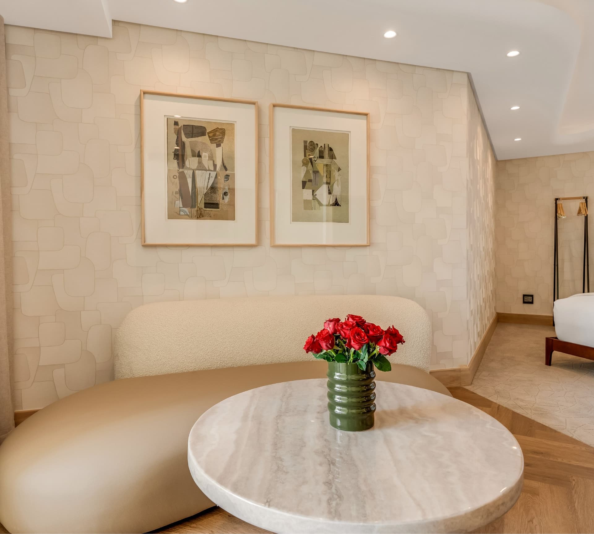 Classic Sea-Facing Room lounge area at The Cole with curved bouclé sofa, marble coffee table, red rose arrangement in a green ceramic vase, and a pair of framed abstract artworks on textured wall