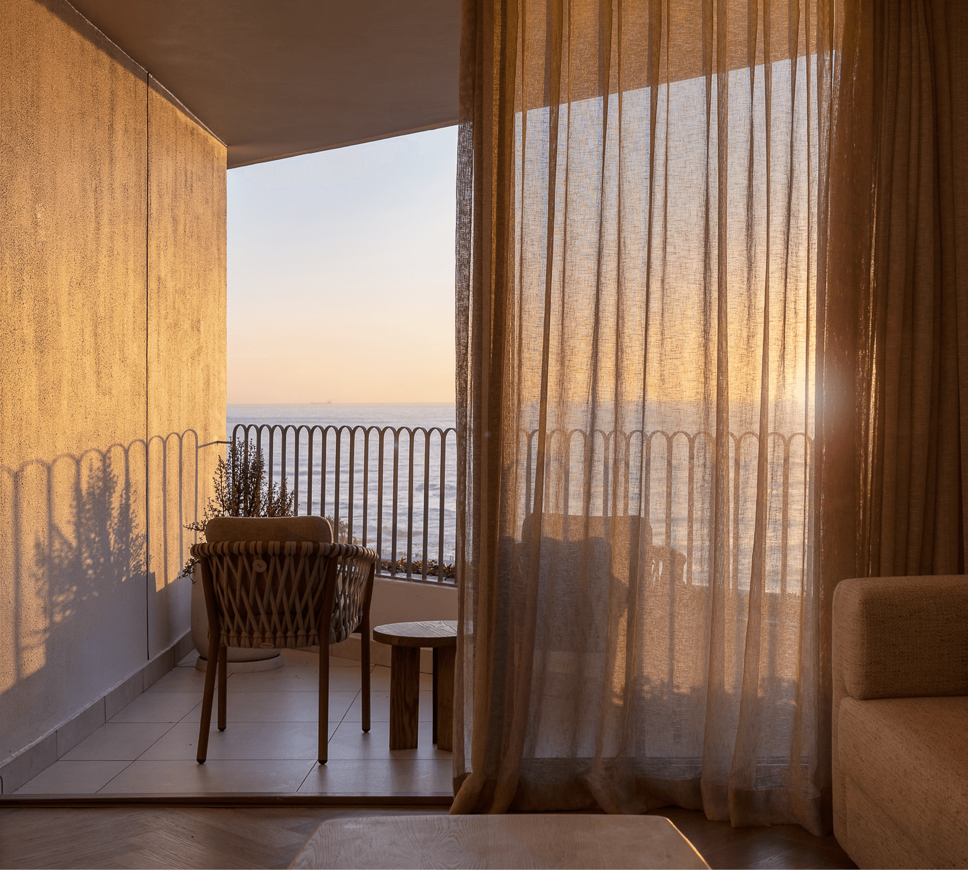 Golden-hour balcony view of the sea from a Superior Sea-Facing Room at The Cole, with woven chair and side table