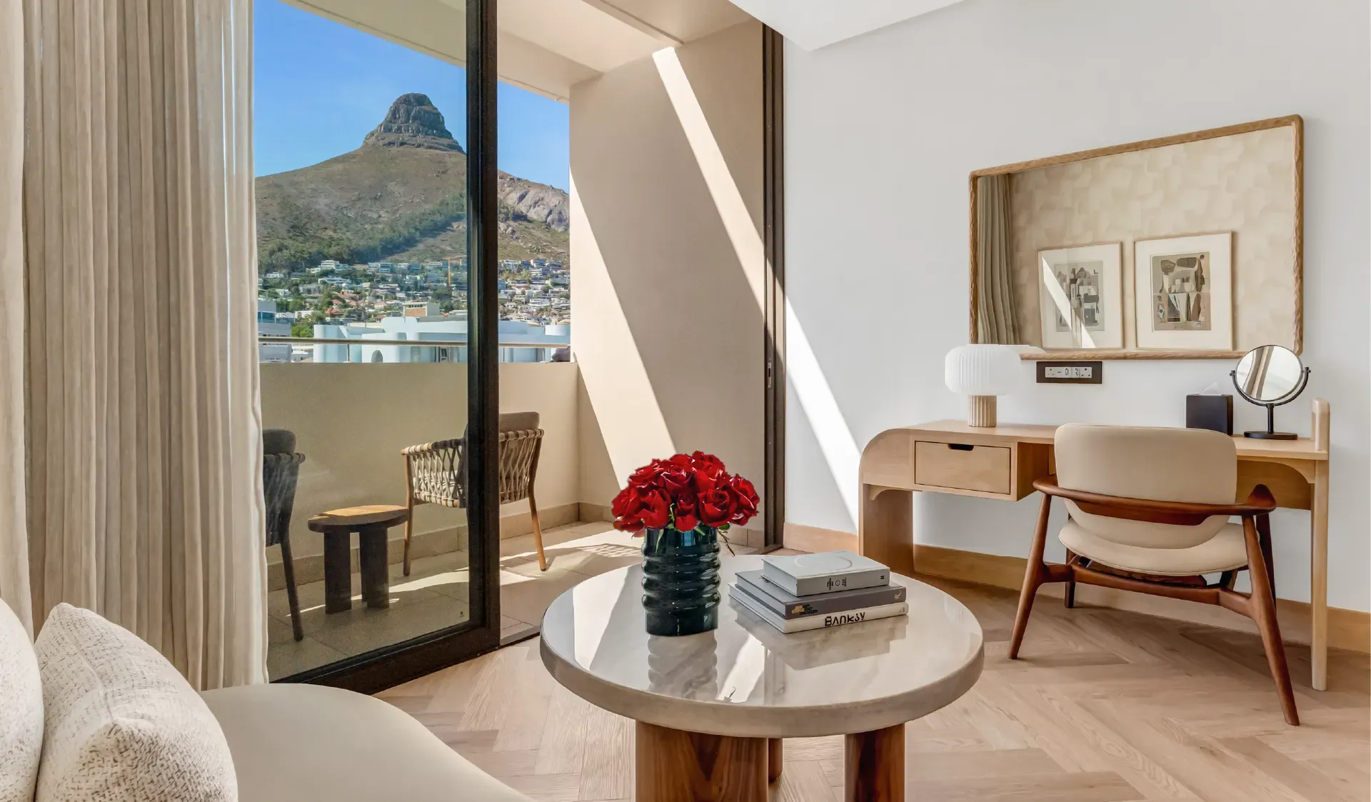 Superior Mountain-Facing Room at The Cole featuring a marble coffee table with red roses and art books, wooden writing desk, and open balcony doors with a direct view of Lion's Head, Cape Town