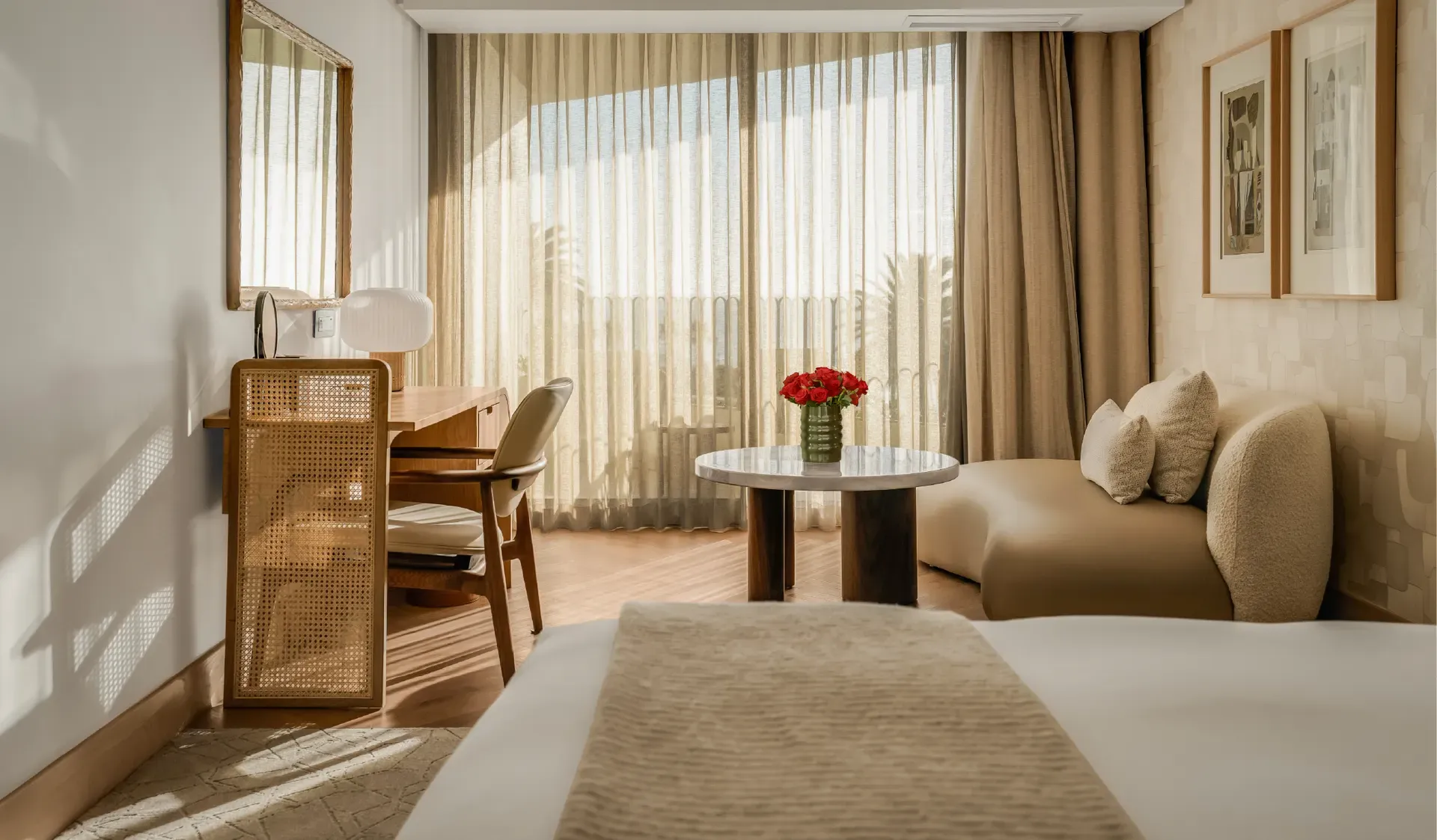 Superior Sea-Facing Room at The Cole with king bed, cane-panelled wardrobe, wooden writing desk, marble coffee table with red roses, curved bouclé sofa, and floor-to-ceiling sheer curtains with palm tree and sea views