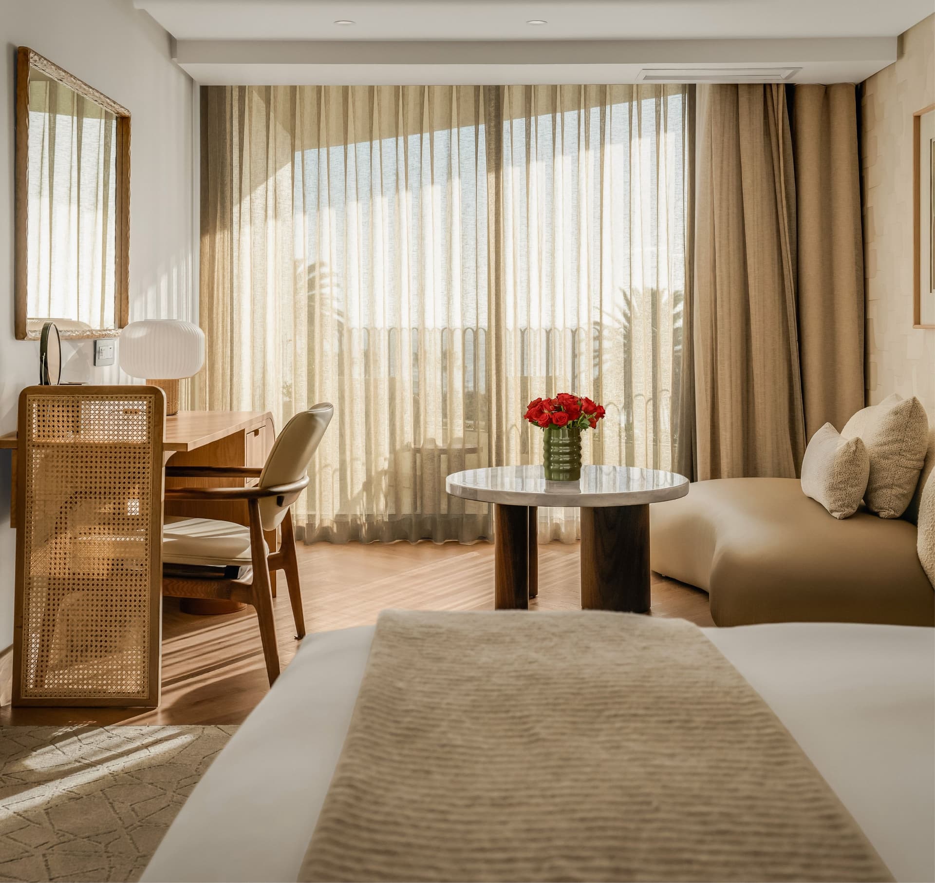 Superior Sea-Facing Room at The Cole with king bed, cane-panelled wardrobe, wooden writing desk, marble coffee table with red roses, curved bouclé sofa, and floor-to-ceiling sheer curtains with palm tree and sea views
