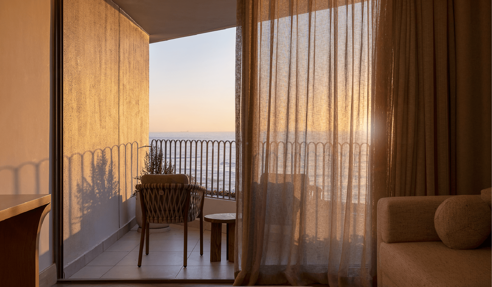 Sunset ocean view through sheer curtains from a Superior Sea-Facing Room balcony at The Cole